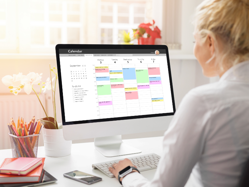 Woman sitting at a desk focused on her computer screen with a digital planner open.