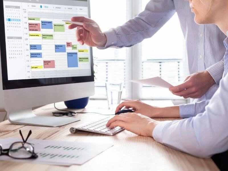 Two colleagues planning time blocking strategies in front of a computer screen