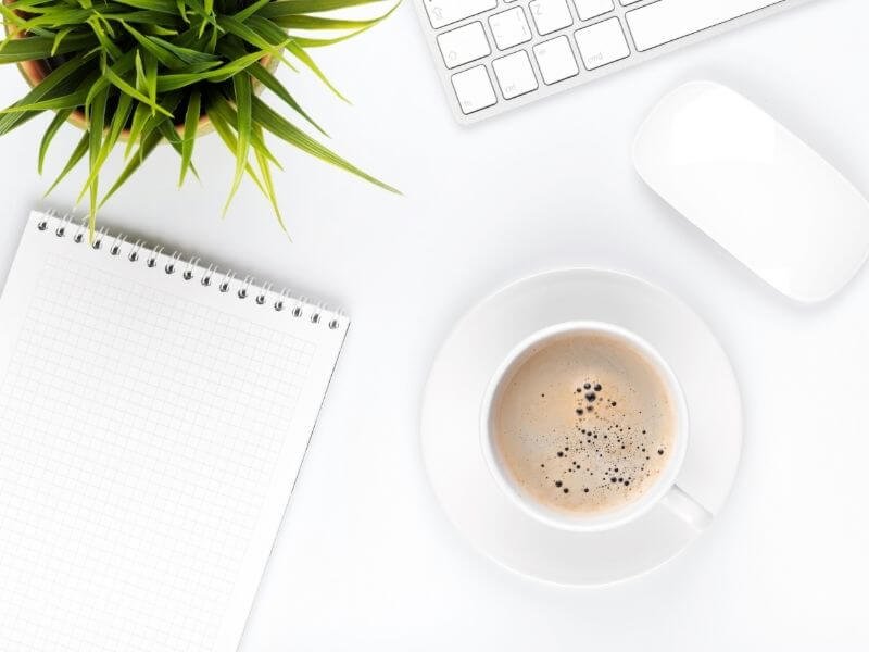 Minimalist workspace with laptop, coffee cup, plant, keyboard, and notebook for productivity