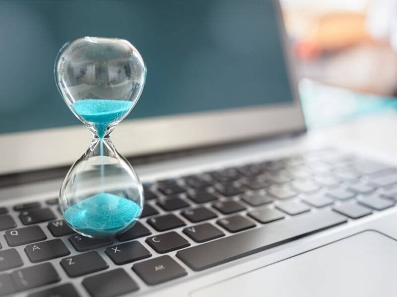 Turquoise hourglass next to a laptop representing time management in online learning